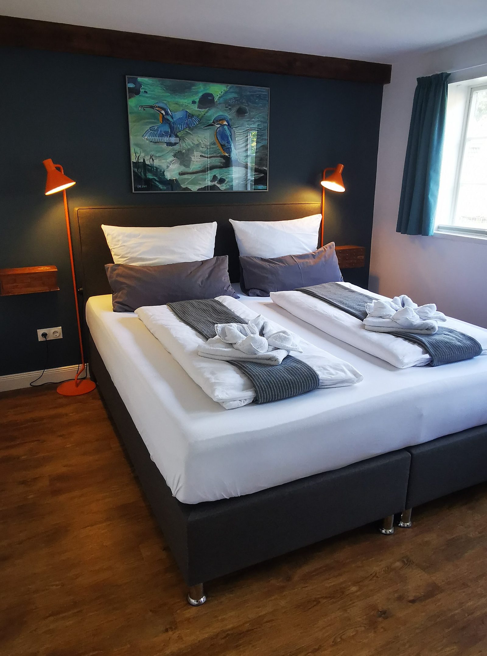 Das Liewermang: Doppelbett vor dunkelblauer Wand mit Bild und zwei Leselampen