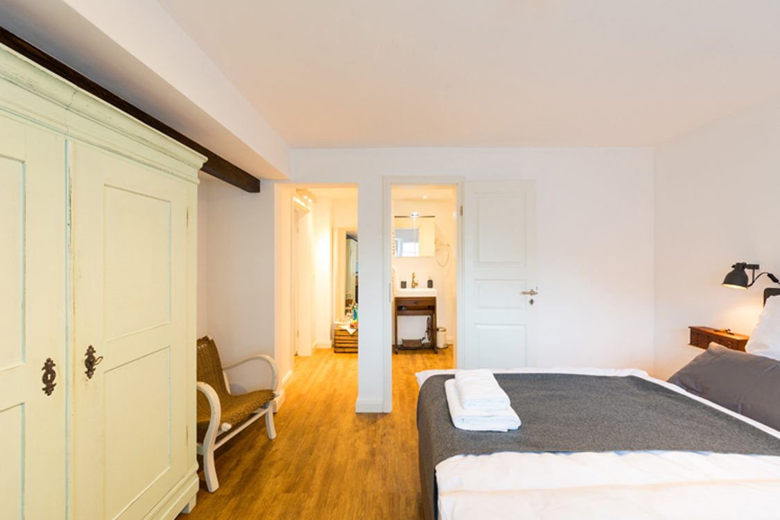 Die Schlieperschmette: helles Zimmer mit Bett, altem Bauernschrank und Blick ins Bad